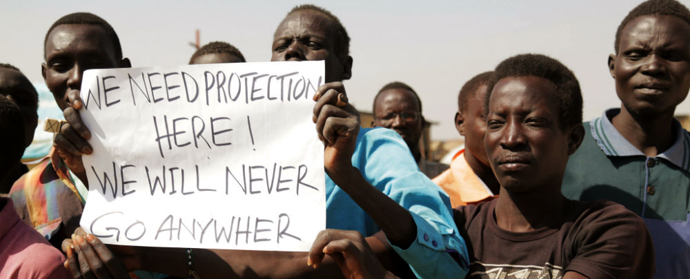 Several South Sudanese hold a sign reading, "We Need Protection Here, We Will Never Go Anywhere"