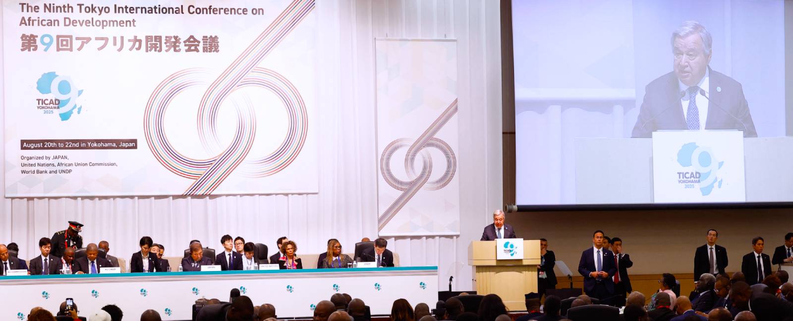 Podium and head table at TICAD 9 as a big screen shows Guterres at podium