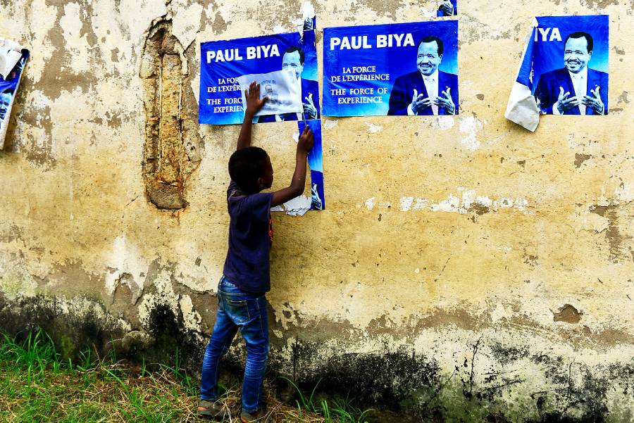 A young child hanging posters of Cameroonian President Paul Biya on a wall in Yaoundé. (Photo: AFP)