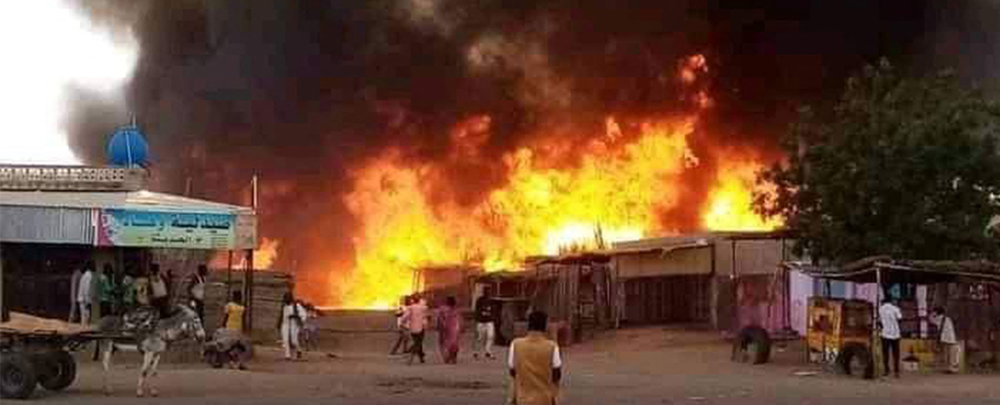 A man stands by as a fire rages in a livestock market area in al-Fasher, the capital of Sudan's North Darfur state, in the aftermath of bombardment by the paramilitary Rapid Support Forces (RSF)