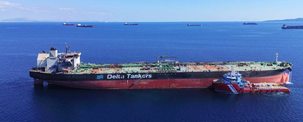 Sounion tanker damaged by Houthi attacks A large tanker ship is guided by tugboat into port, while other tankers wait in the background.