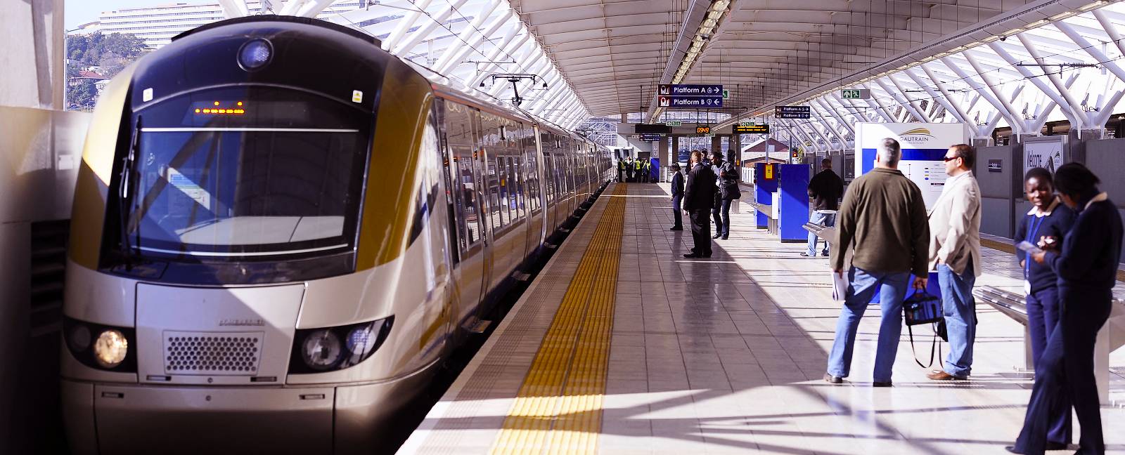 Gautrain A train pulls into a station as passengers wait on the platform.
