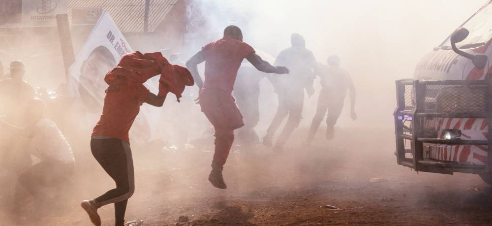 Supporters of Bobi Wine run and cover their heads as the air fills with tear gas.