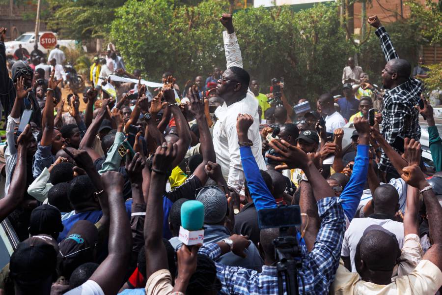 Hundreds of Malians stand in a street and raise fists in the air.