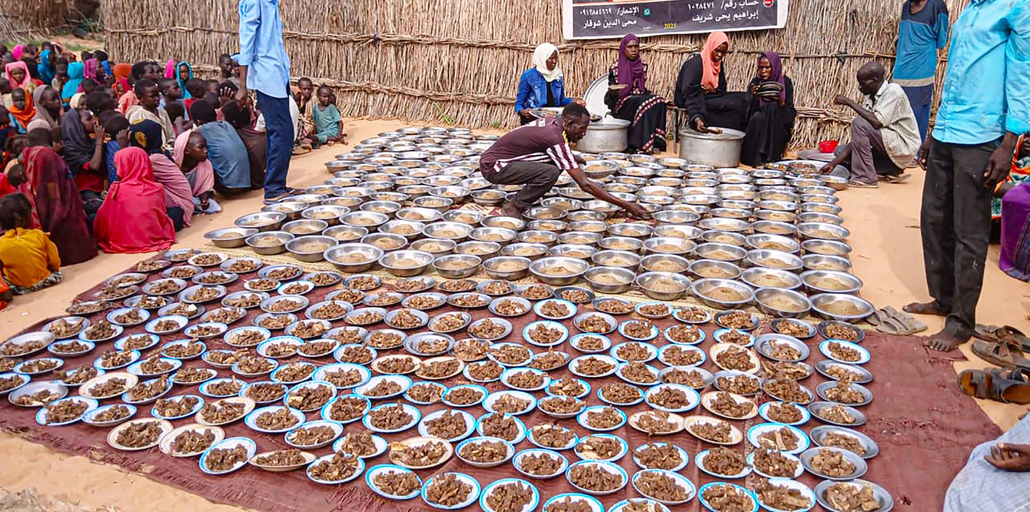 Hundreds of plates are set out by volunteers while residents of Al Fasher wait off to the side.