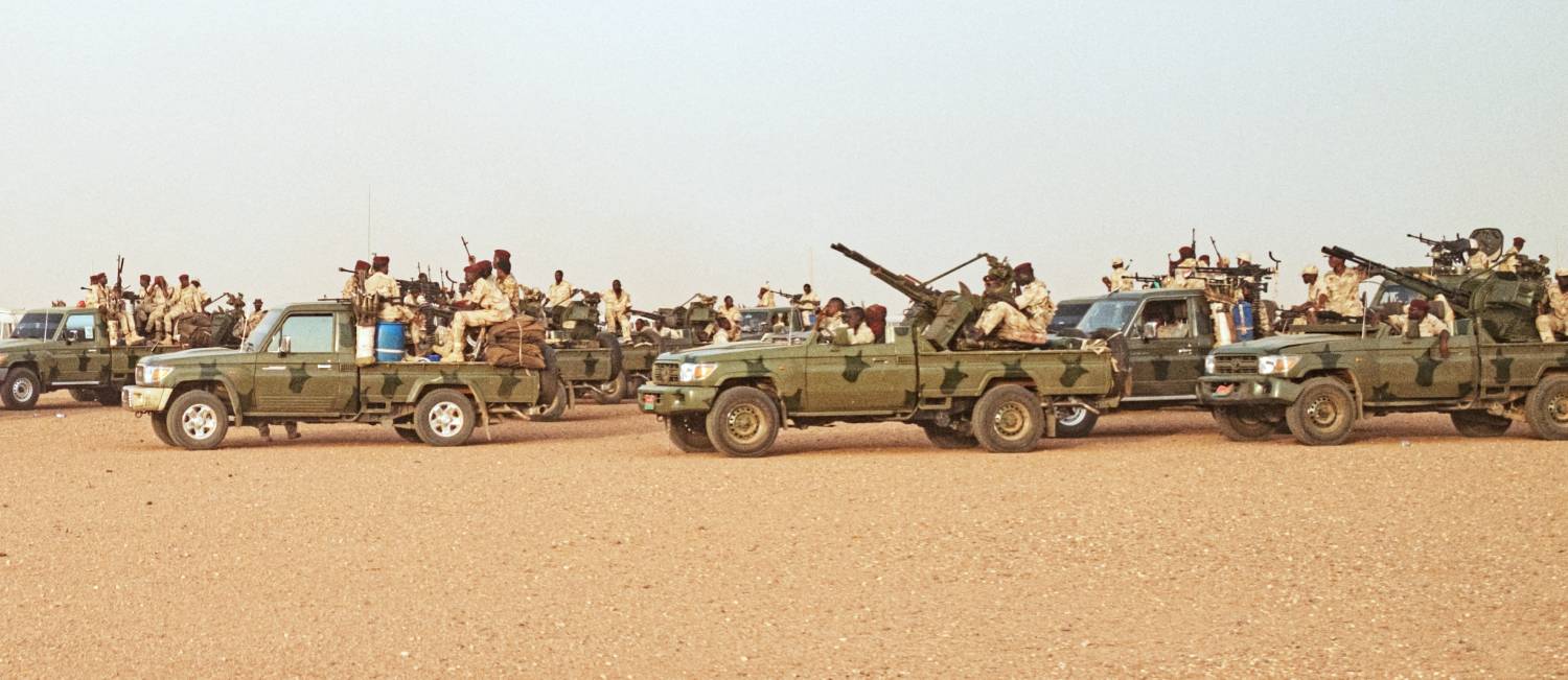 A line of military vehicles full of fighters stretches right to left along the horizon
