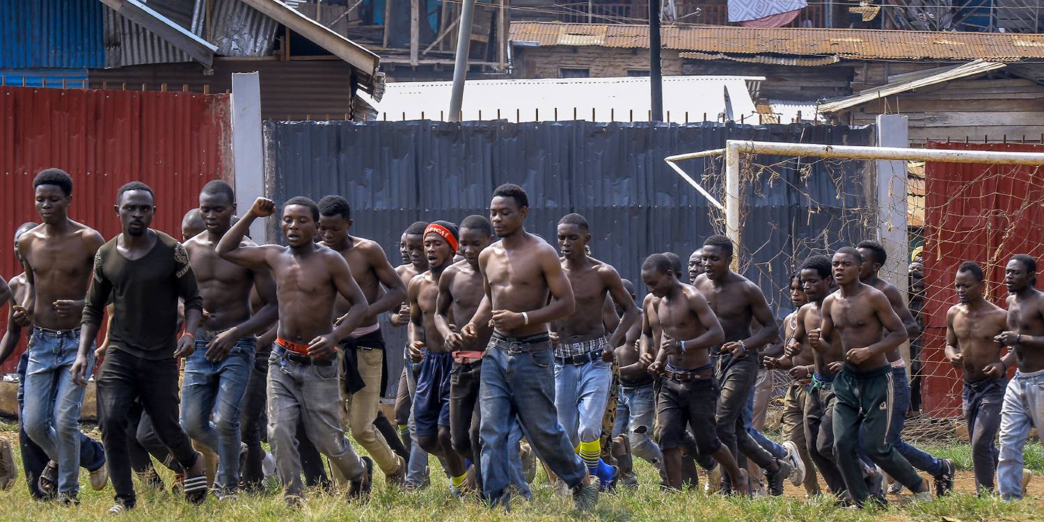 Wazalendo volunteers About two dozen young men in civilian clothes run as a group across a field.